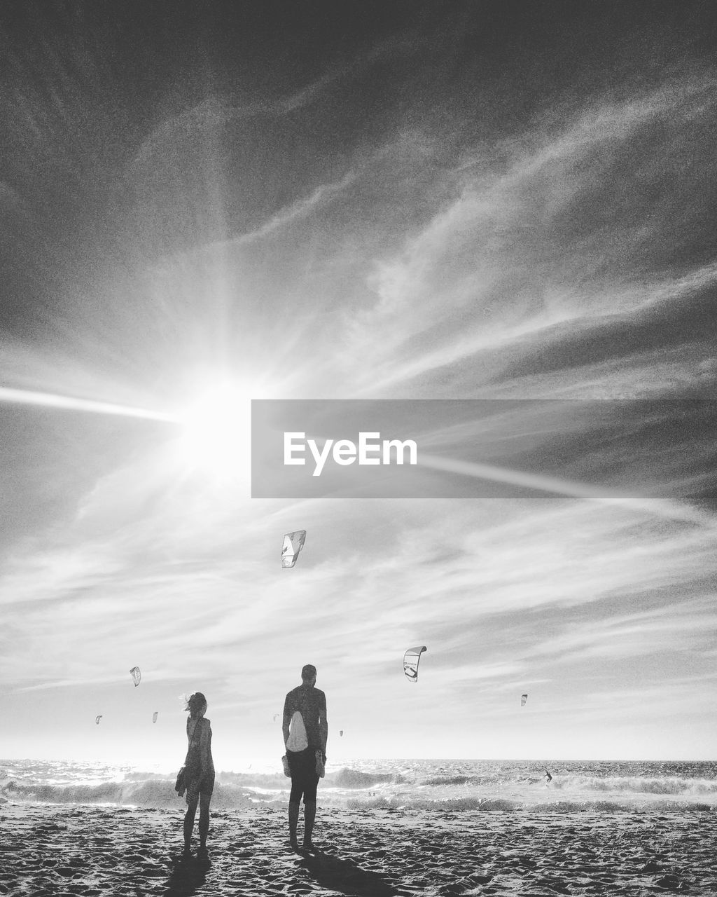 Rear view of man and woman standing at beach against sky on sunny day