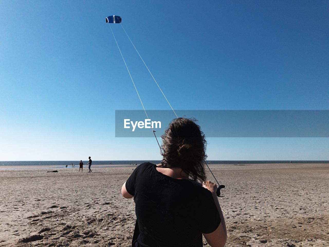 Rear view of woman flying kite on beach against clear blue sky