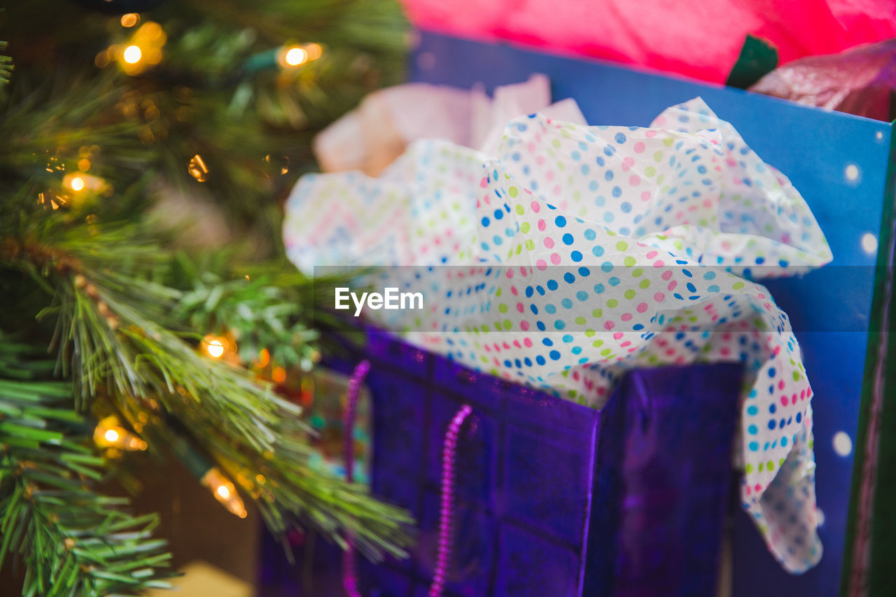 Colorful gift bag with wrapping paper near a christmas tree.