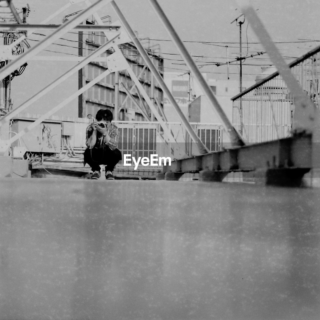 Man photographing while crouching on bridge