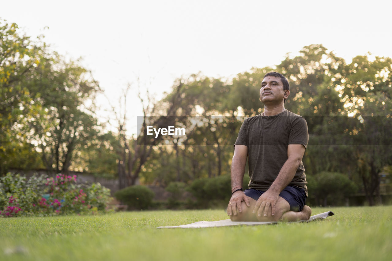 Mid-aged man doing yoga in a park covered with trees on international yoga day.