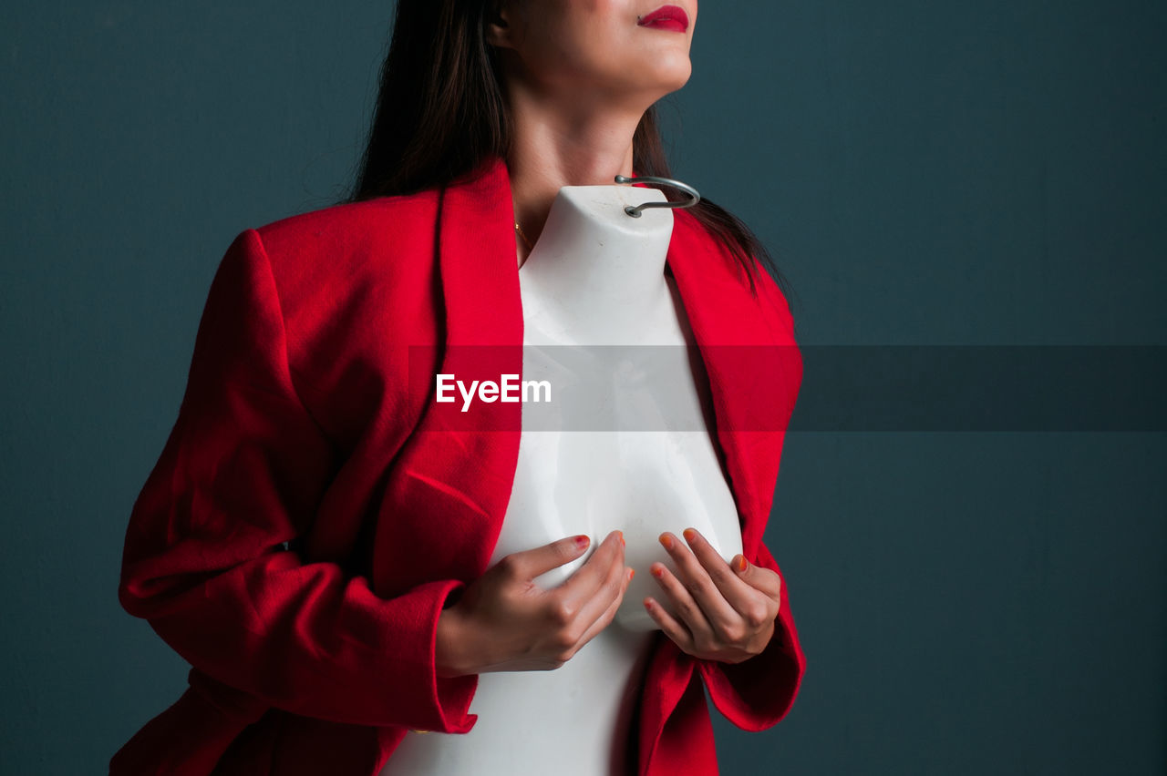 Midsection of woman with mannequin standing against wall