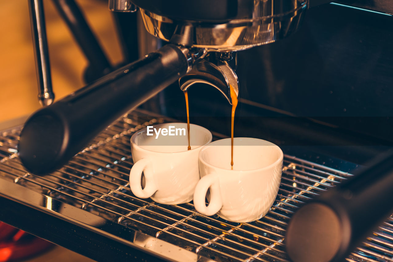 Close-up of drink pouring in cups on espresso maker