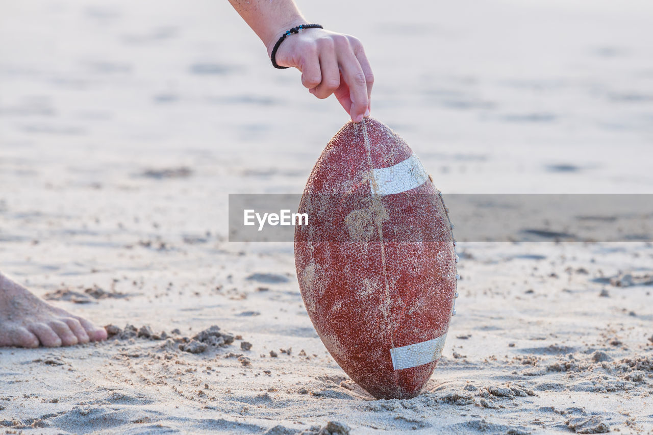 Cropped hand of man holding rugby ball on sand at beach