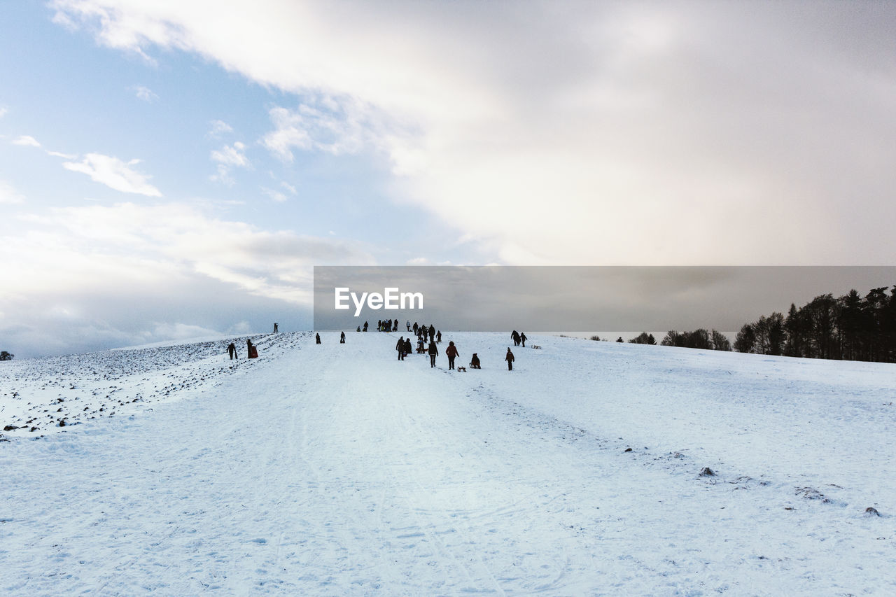 People on snowy landscape against sky during winter