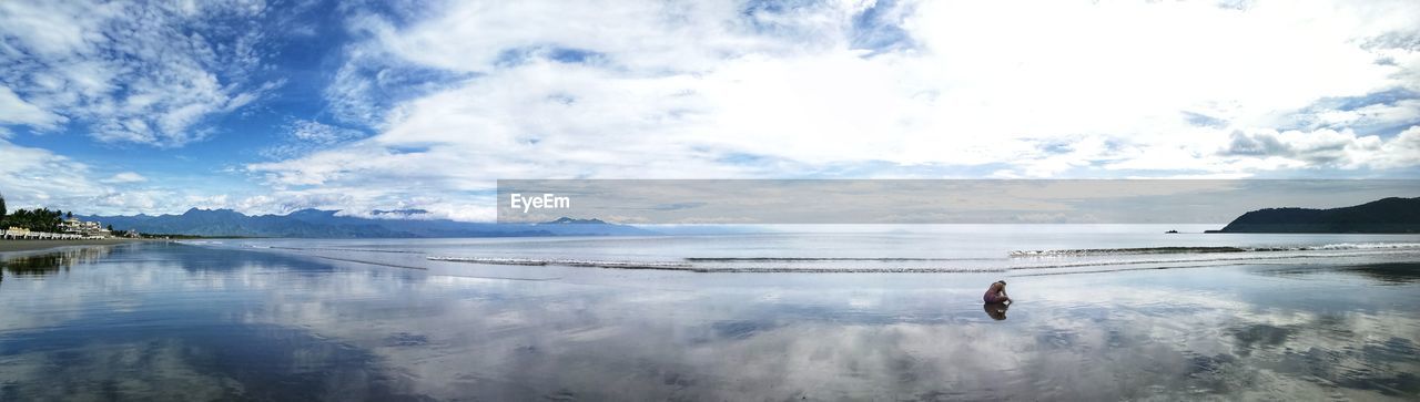 PANORAMIC VIEW OF MAN STANDING IN SEA AGAINST SKY