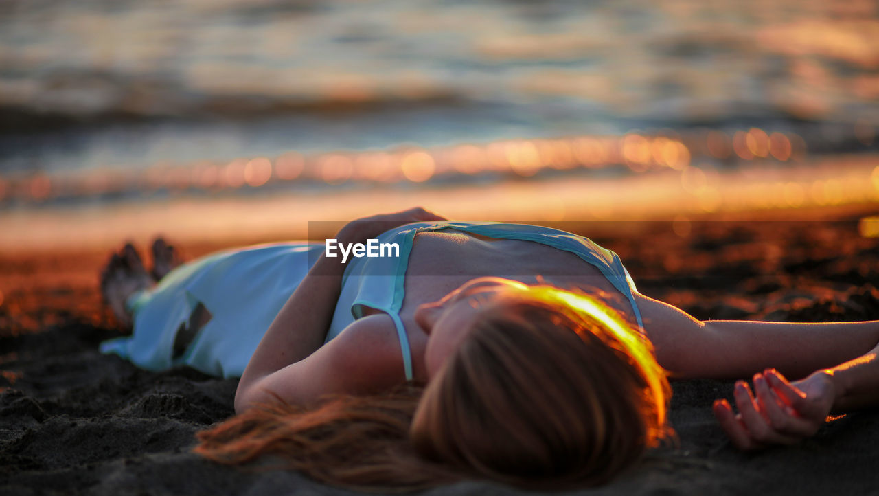 Young woman lying on beach during sunset