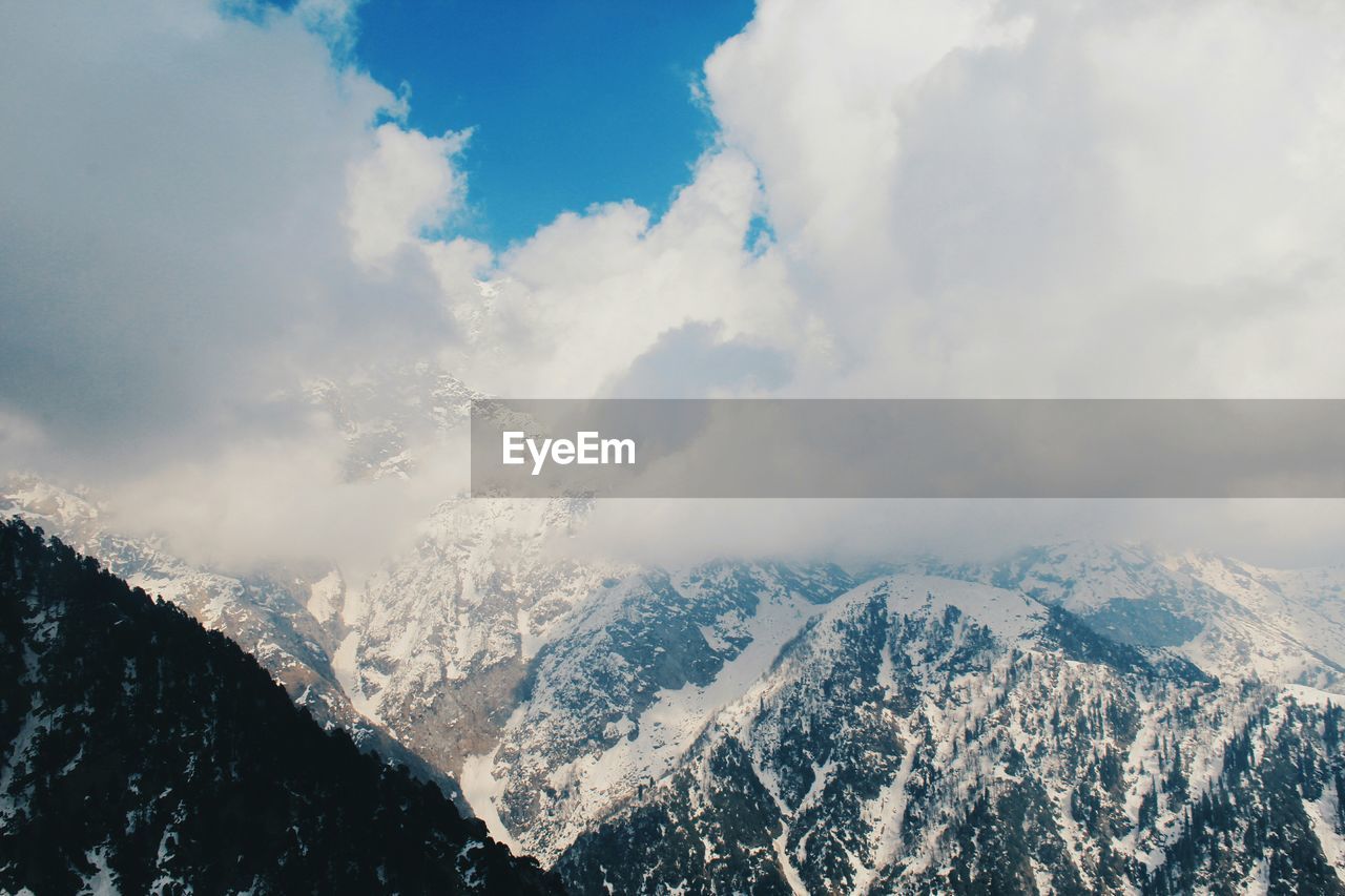 Scenic view of snow covered mountains against cloudy sky