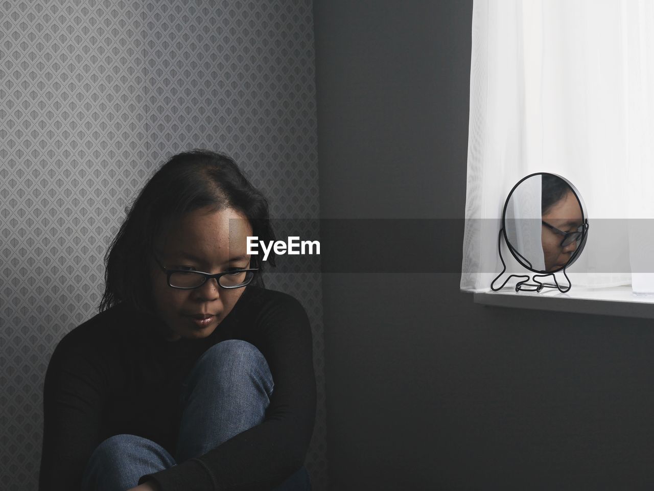 Thoughtful woman with reflection in mirror sitting at home