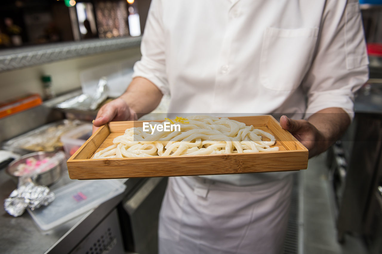 Midsection of chef holding tray of noodles