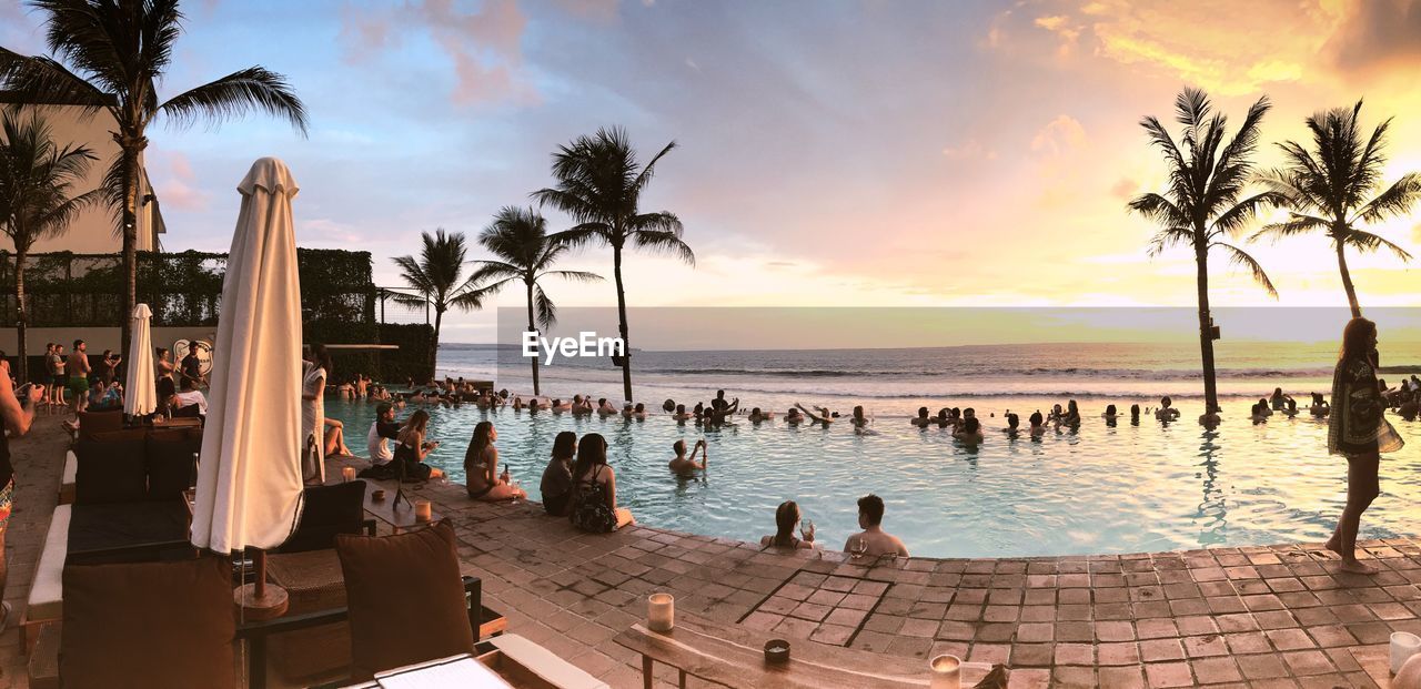 GROUP OF PEOPLE AT SWIMMING POOL AGAINST SKY