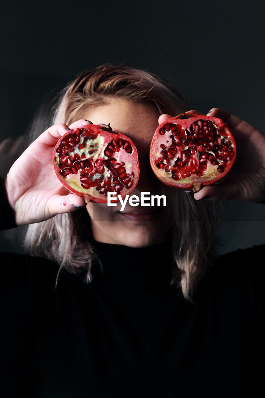 Woman holding halved pomegranate against black background