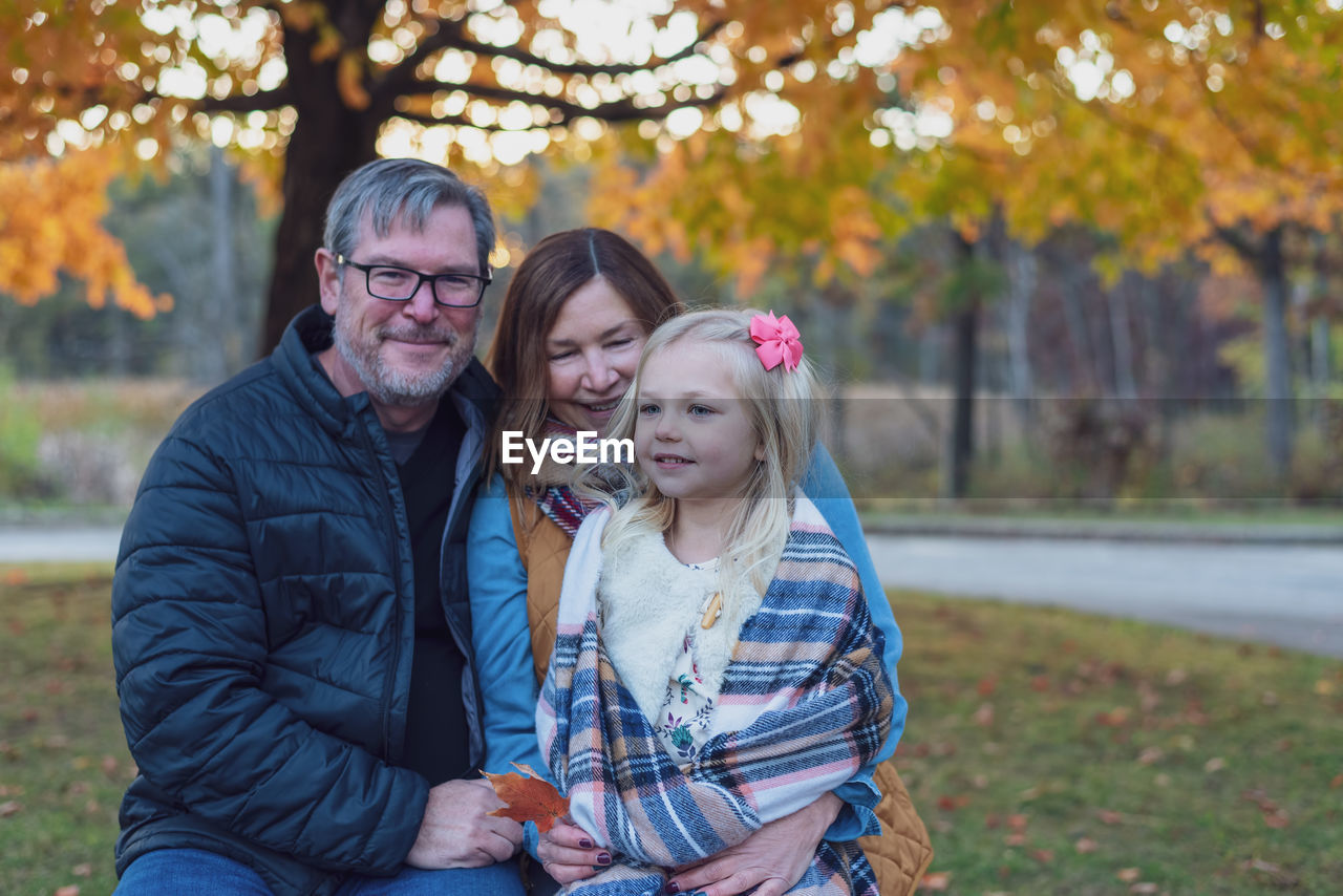 Portrait of happy family sitting at park during autumn