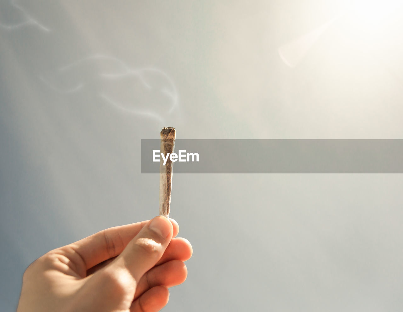 CLOSE-UP OF HAND HOLDING CIGARETTE AGAINST WHITE BACKGROUND