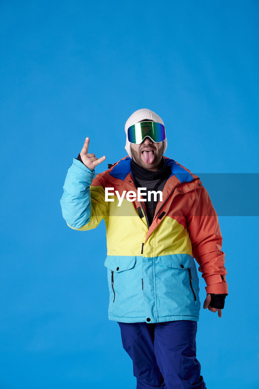 blue, one person, sports, adult, clothing, men, portrait, standing, ski goggles, sky, young adult, front view, emotion, leisure activity, winter, nature, sports equipment, cold temperature, looking at camera, extreme sports, winter sports, sports clothing, helmet, happiness, activity, copy space, person, mountain, colored background, day, sports helmet, athlete, snow, fun, three quarter length, outdoors, snowboarding, clear sky