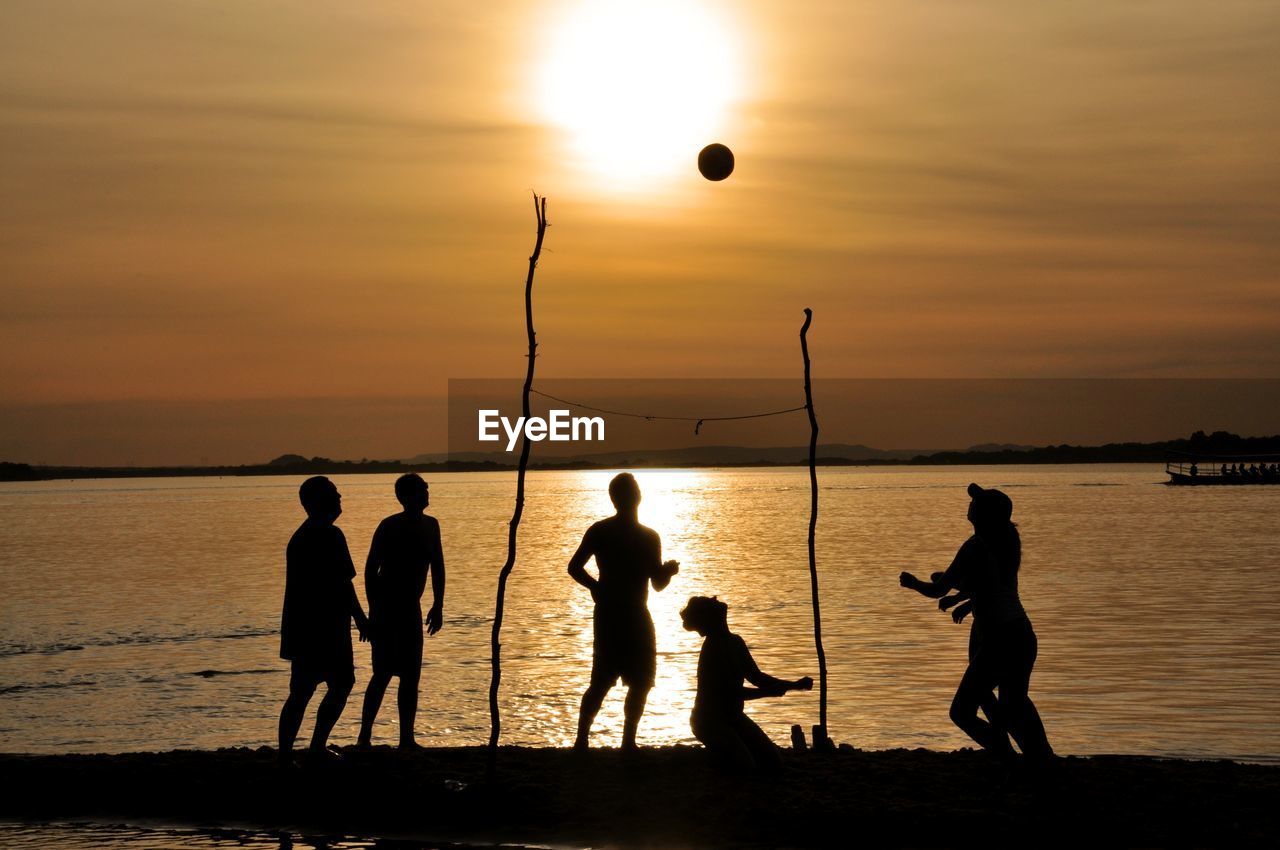 Silhouette people playing with ball on beach against sky during sunset