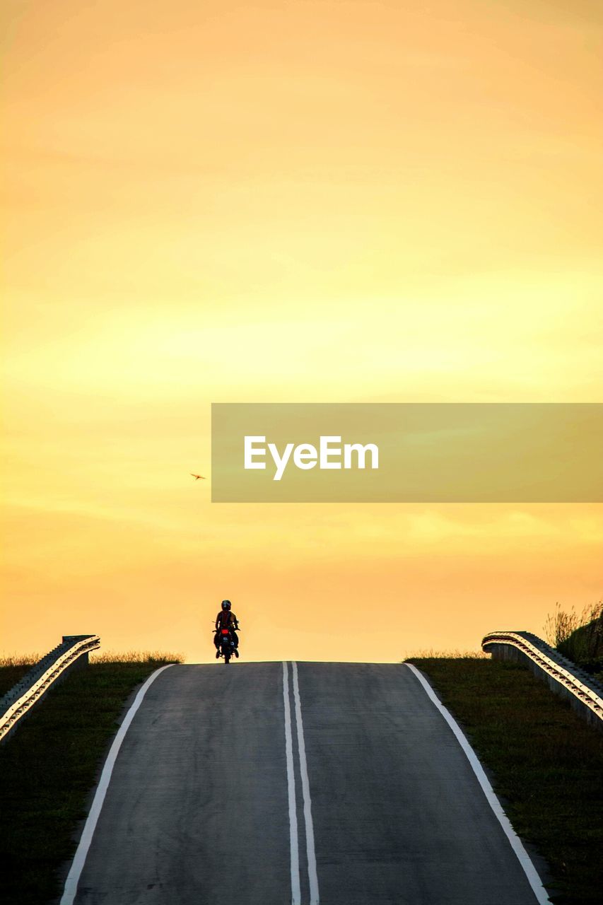 Person riding motorcycle on country road against sky during sunset