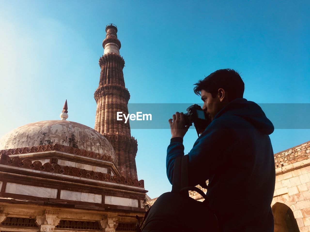 Low angle view of young man photographing mosque against clear blue sky