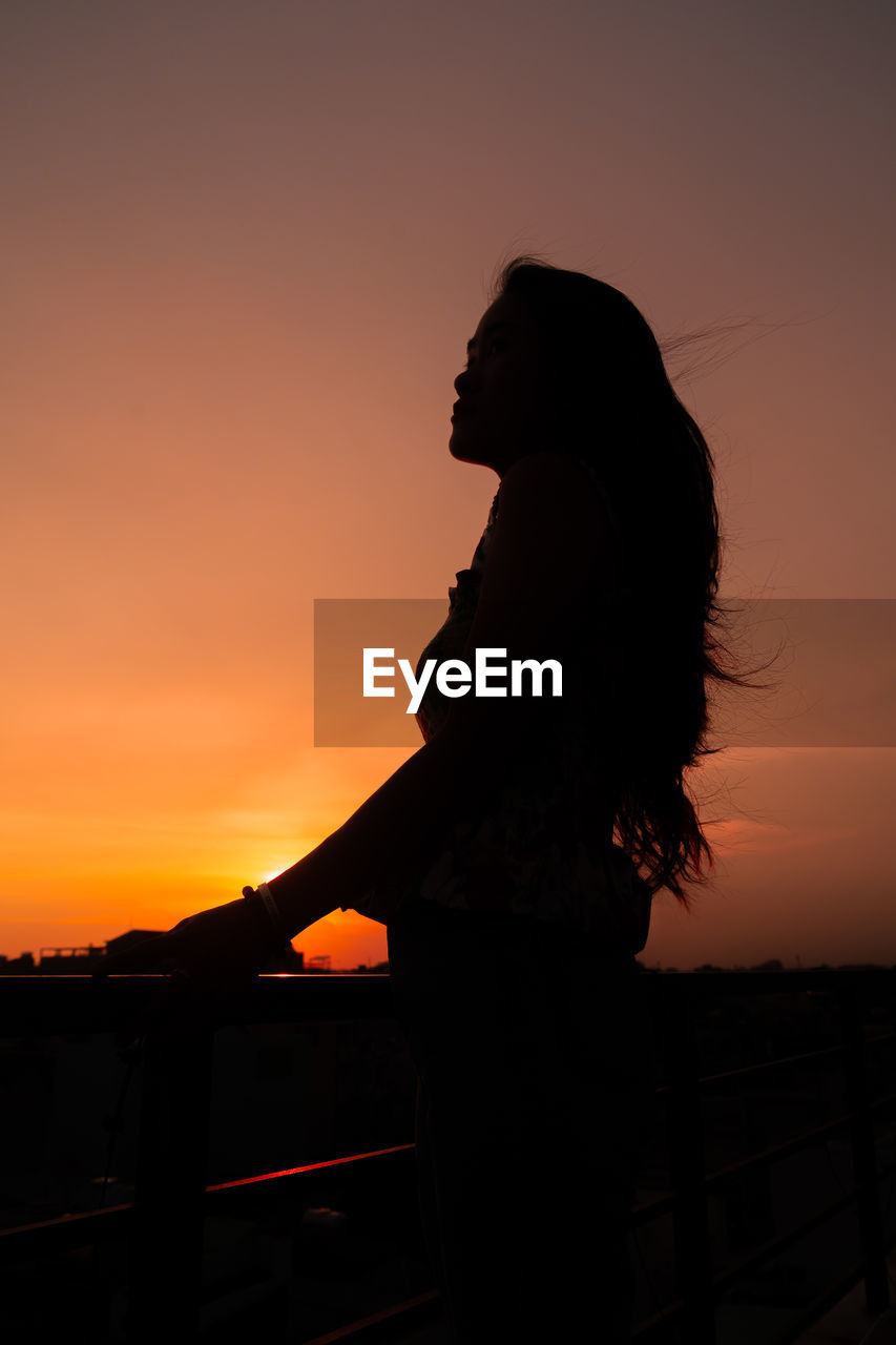 SILHOUETTE WOMAN STANDING AGAINST SKY DURING SUNSET