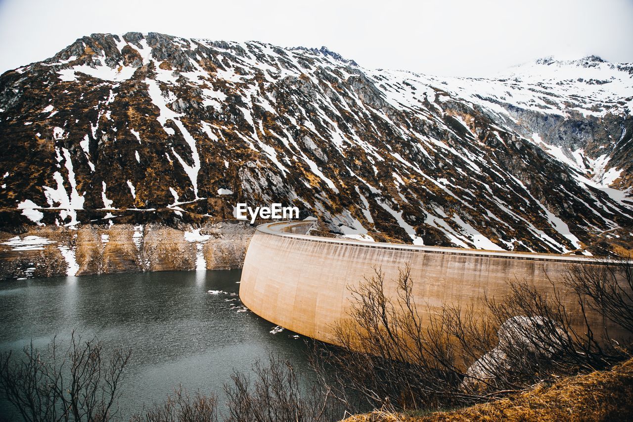 Scenic view of snow covered mountain with dam against sky