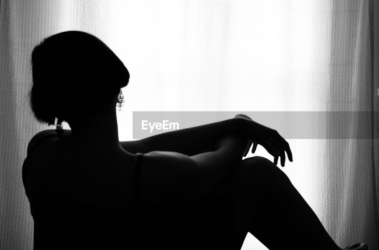 Woman sitting by curtain at home