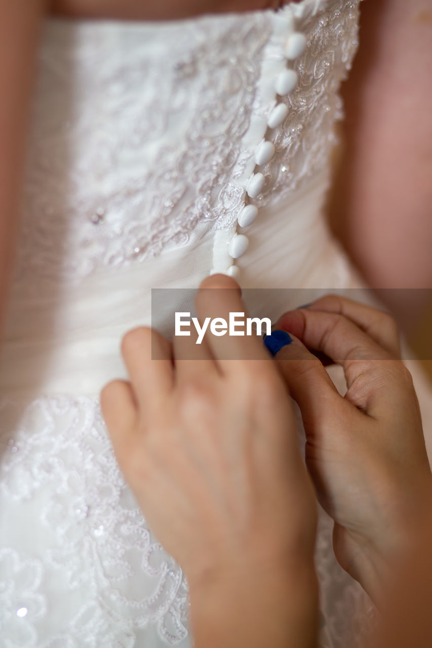 Cropped hands of woman assisting bride in getting dressed