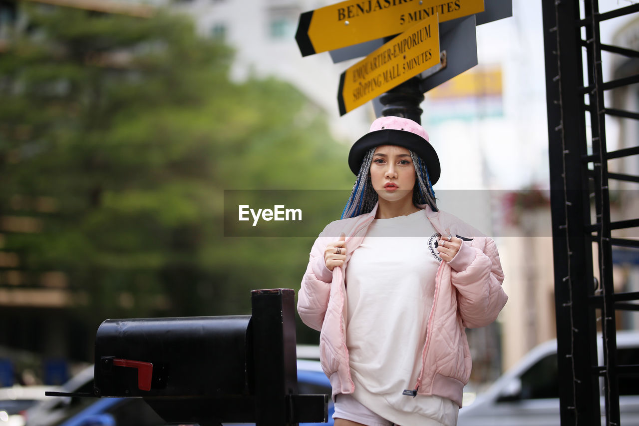 Portrait of young woman standing by street sign outdoors