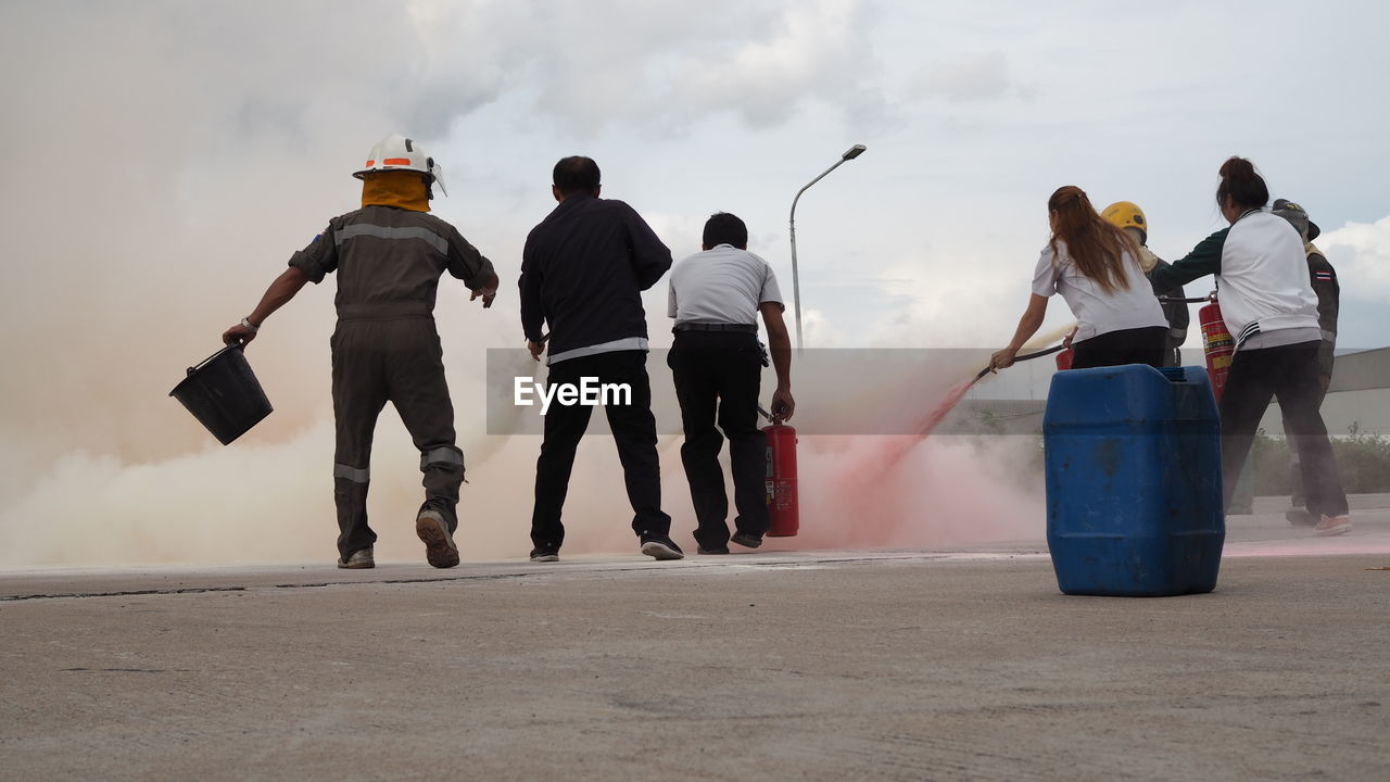 Rear view of people spraying water on fire against sky