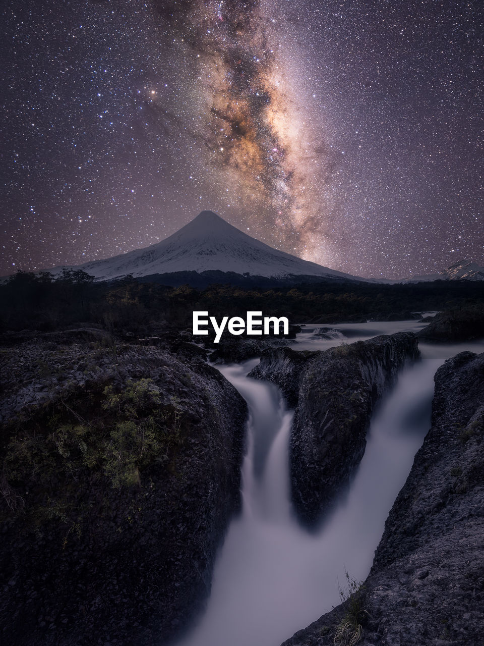 Scenic view of waterfall by mountains against star field at night