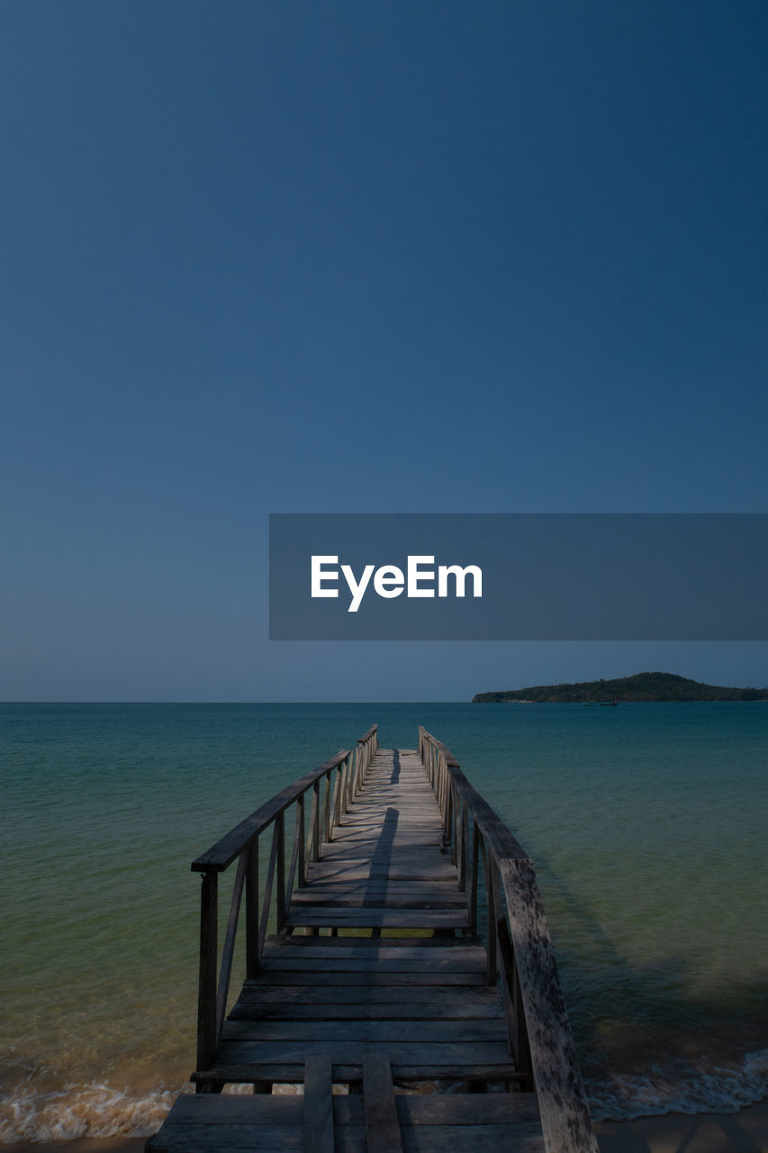 Pier over sea against clear blue sky