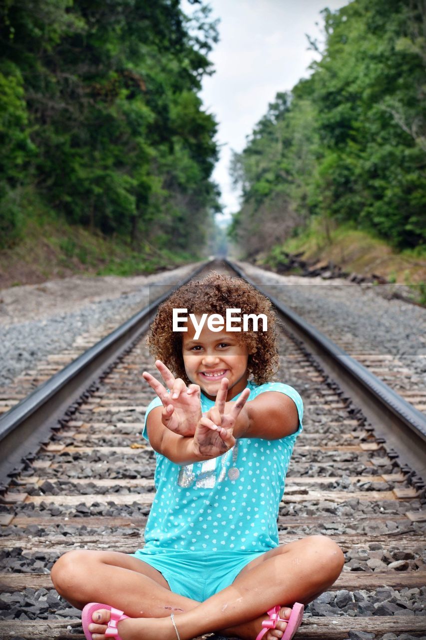 PORTRAIT OF HAPPY GIRL SITTING ON RAILROAD TRACK