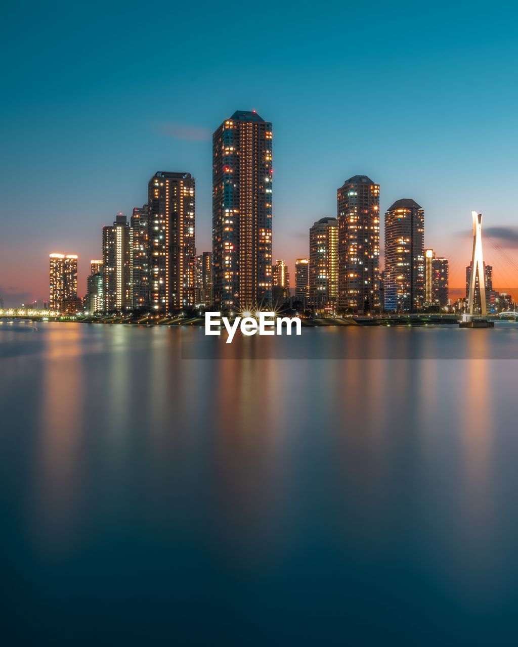 Sea by illuminated buildings against sky at night