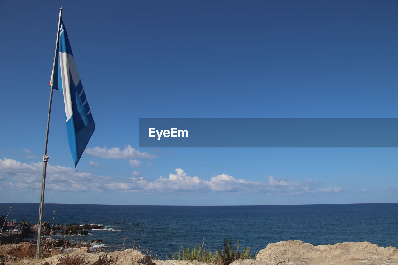 sky, water, sea, nature, flag, blue, beach, ocean, land, scenics - nature, beauty in nature, horizon, horizon over water, wind, environment, tranquility, no people, day, tranquil scene, patriotism, coast, clear sky, outdoors, vacation, cloud, sunlight, body of water, copy space, shore, pole, sunny, non-urban scene