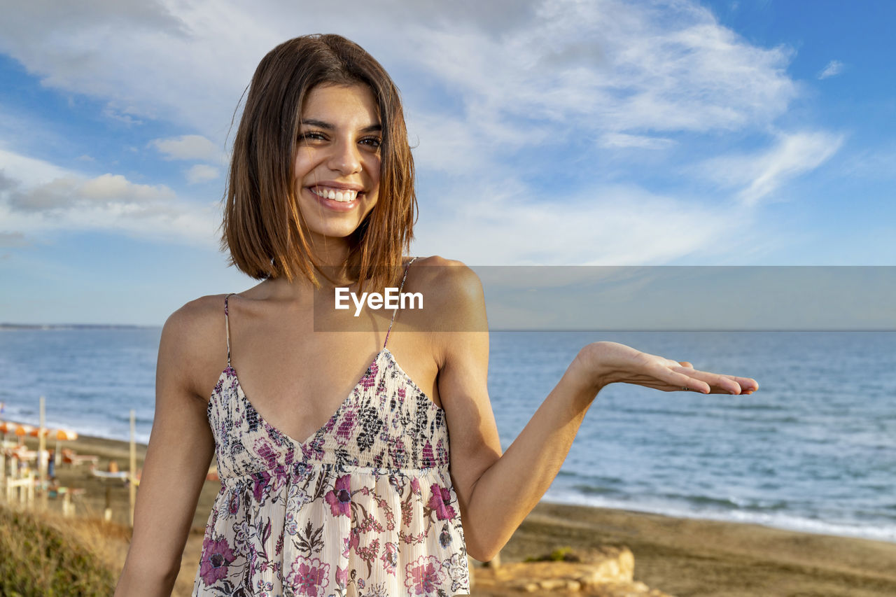 Smiling girl raising up her left hand to show a potential copy space on the right. 