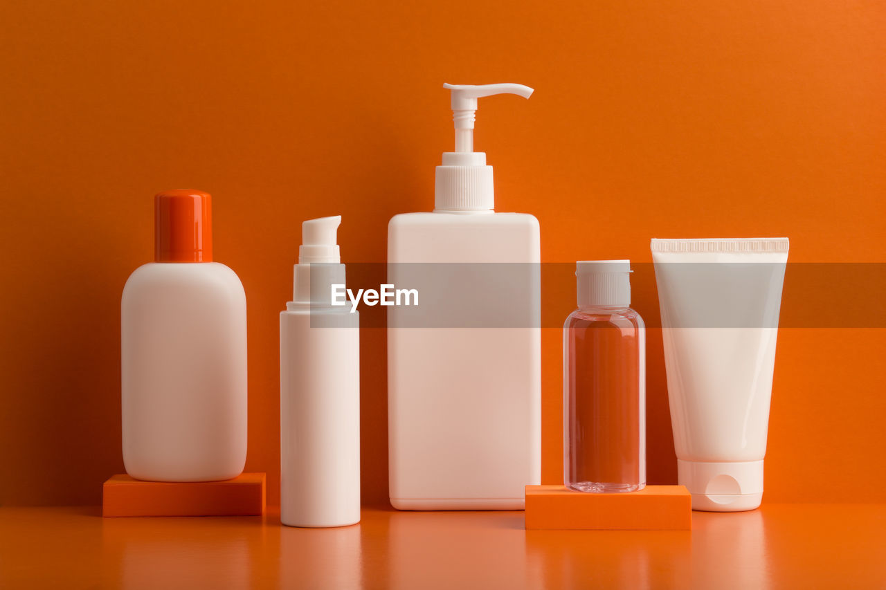 Close-up of unbranded cosmetic bottles on orange background