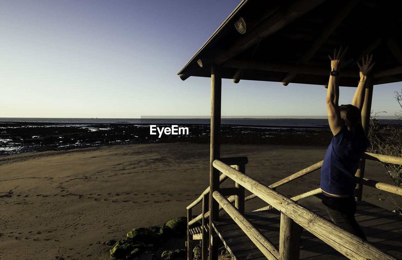 Man exercising on wooden structure at beach