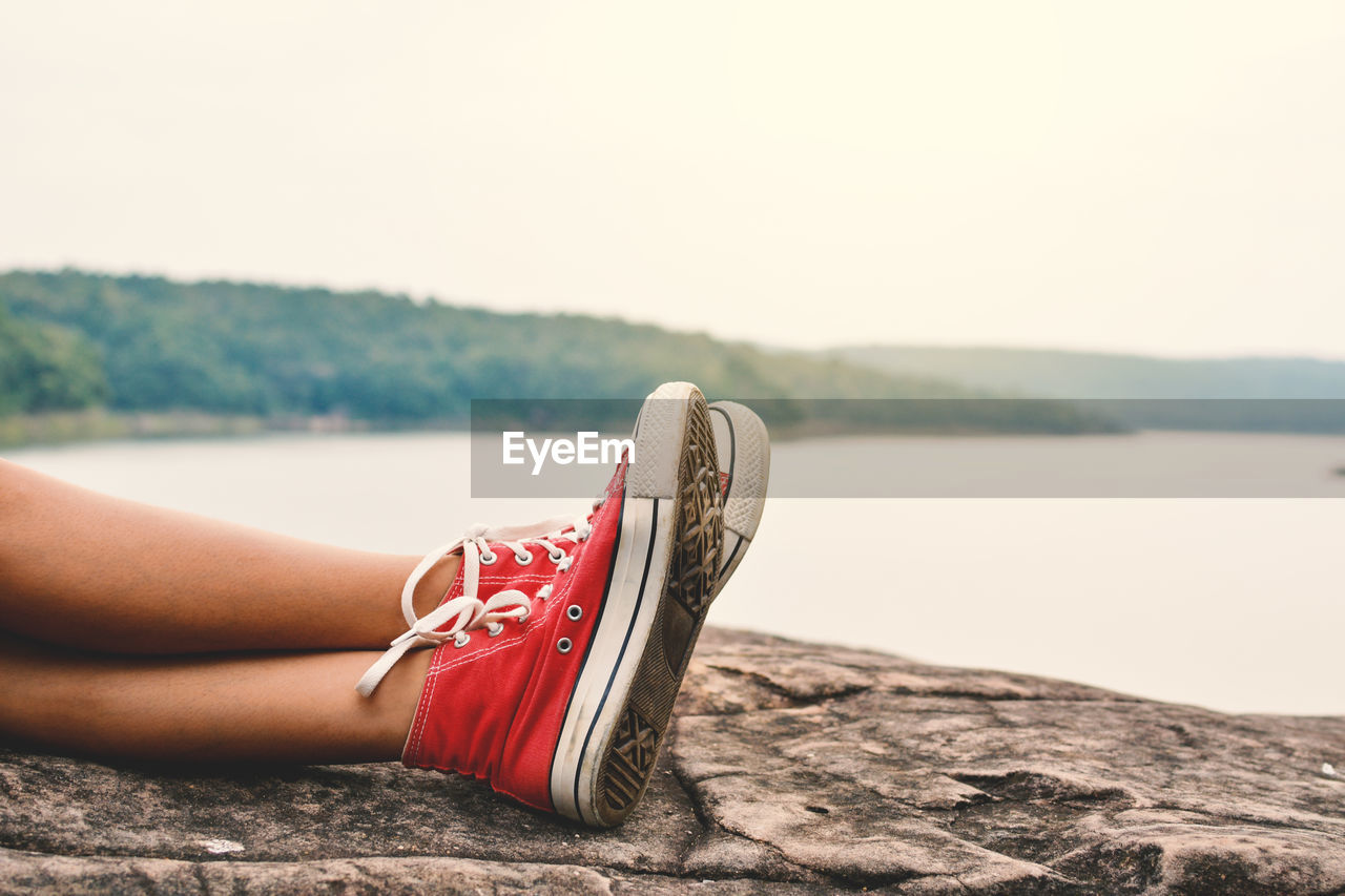 Low section of woman lying on rock by lake against sky