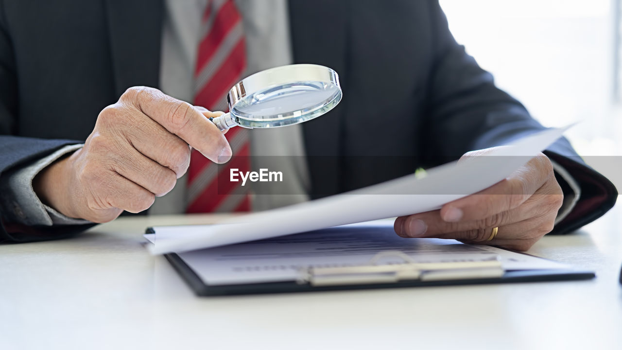 Midsection of lawyer examining paper through magnifying glass on desk