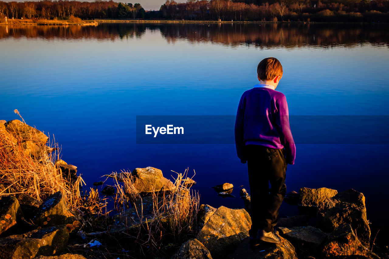 Rear view of boy looking down standing by lake