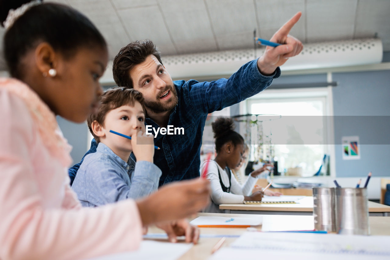 Teacher discussing with boy while pointing in classroom at school