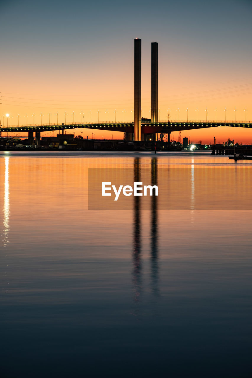 Scenic view of river by illuminated buildings against sky during sunset