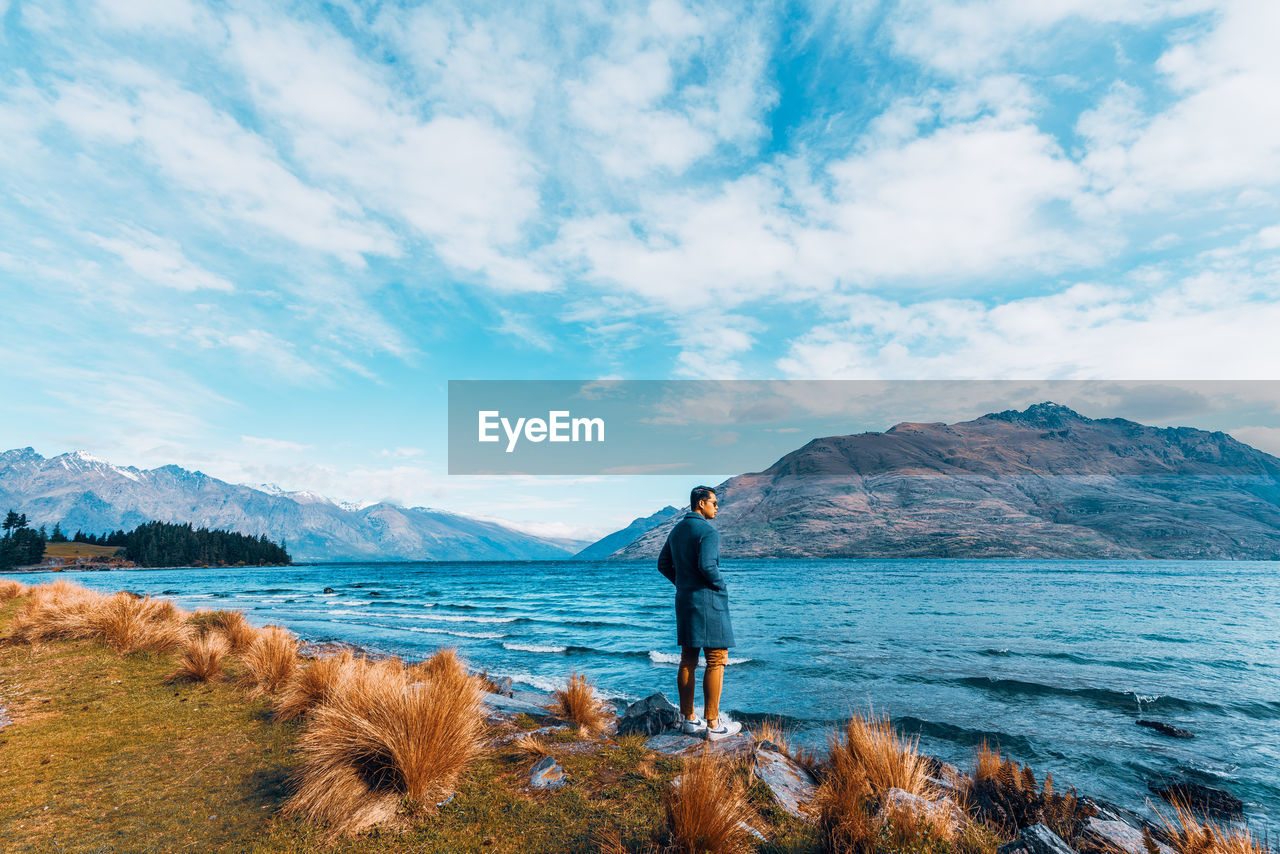 REAR VIEW OF MAN LOOKING AT VIEW OF MOUNTAINS