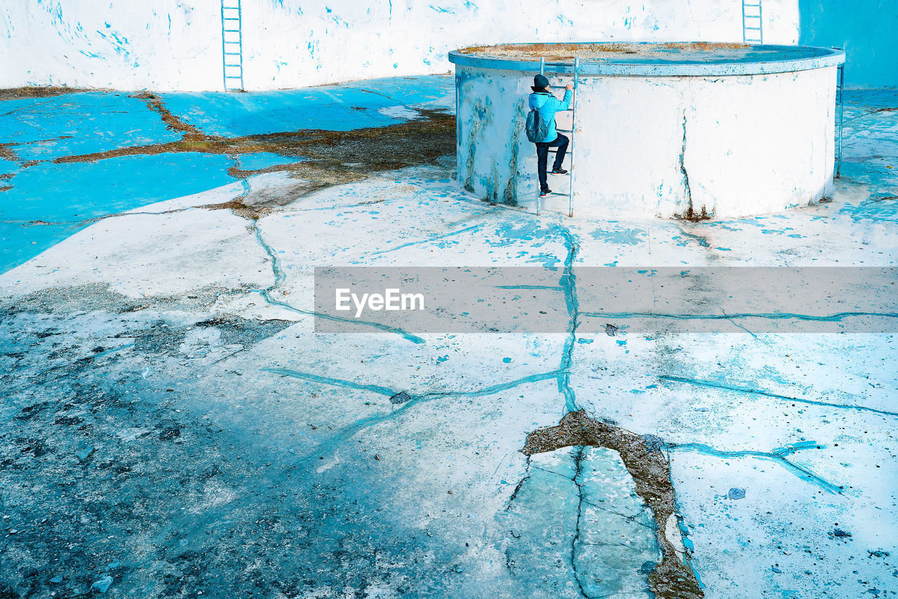 Man climbing stairs on abandoned blue pool