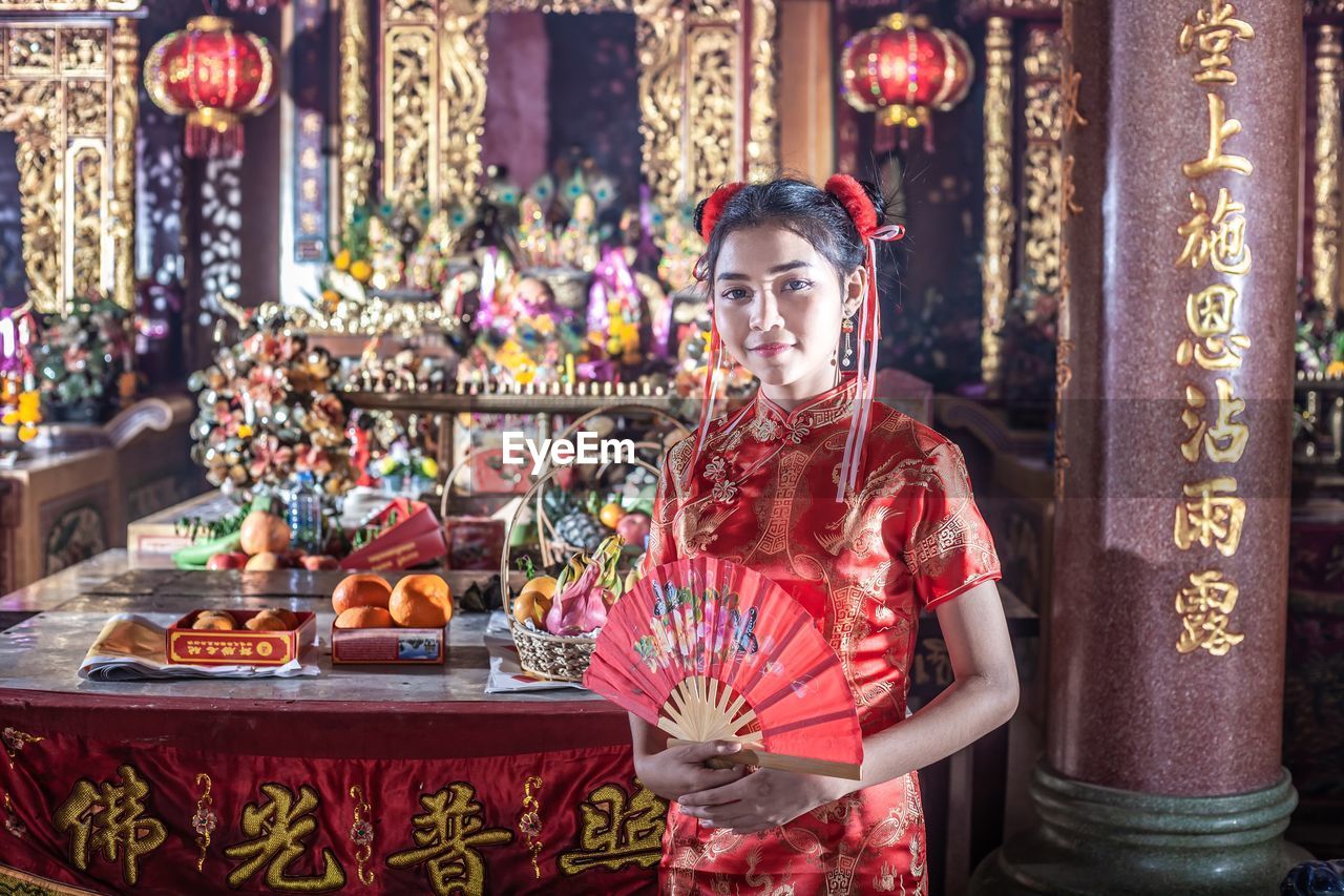 Portrait of teenager holding hand fan standing at temple