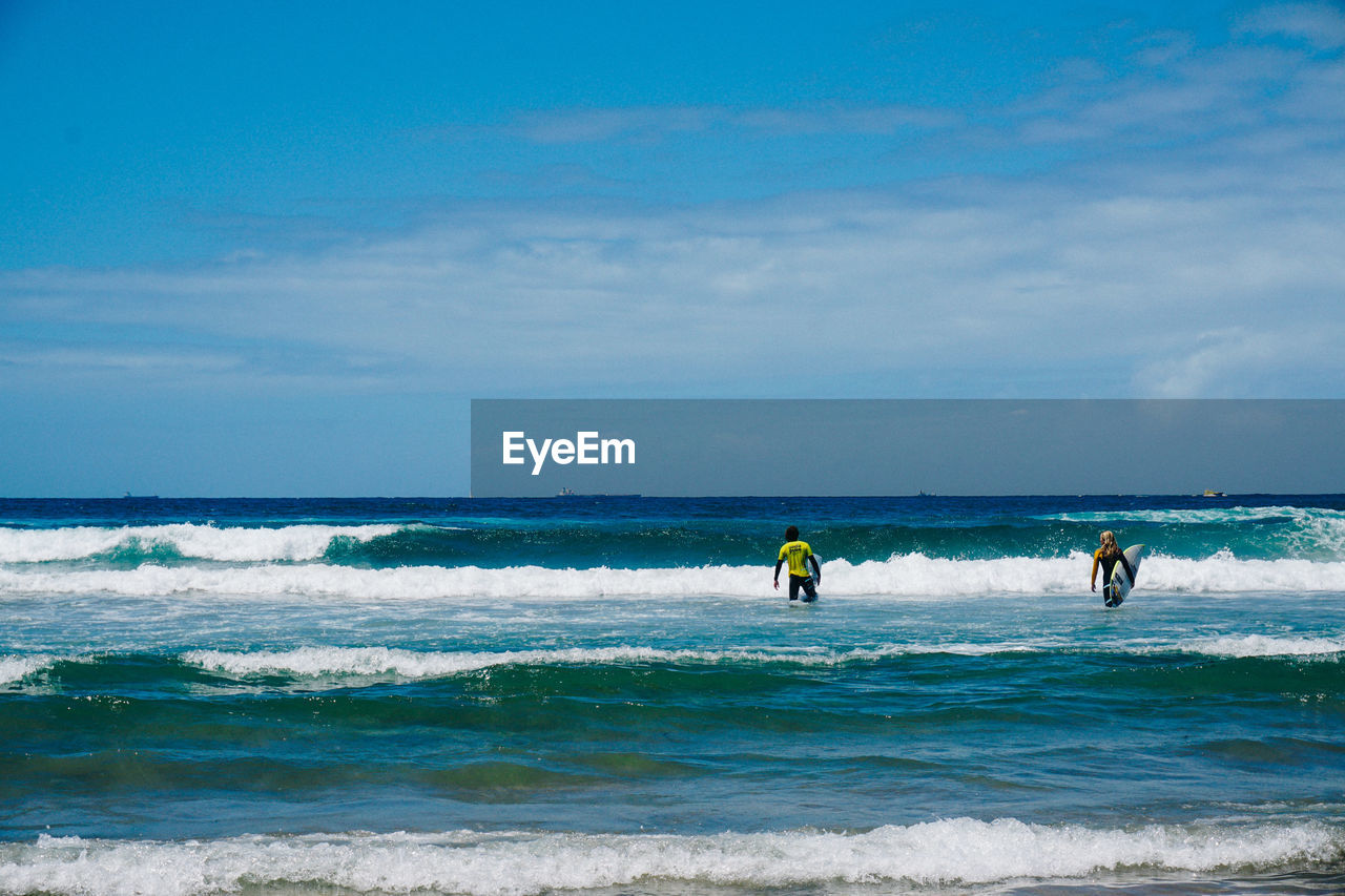 Rear view of friends with surfboards walking in sea against sky