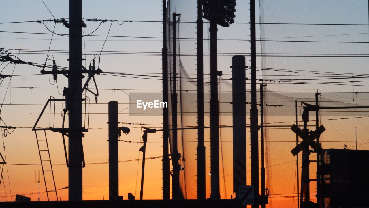 Silhouette electricity pylons against sky during sunset