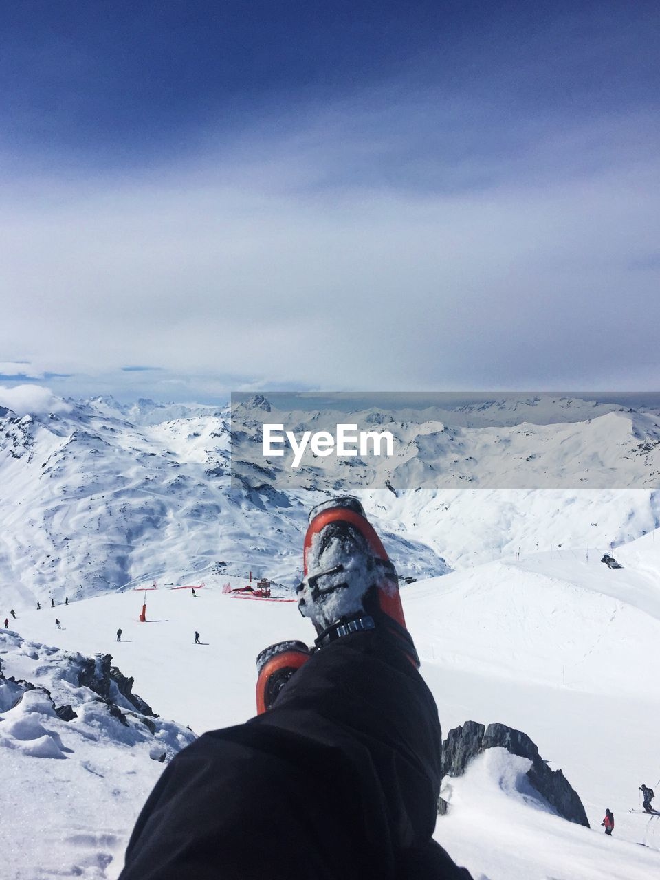 Low section of man resting on snow covered mountain against sky