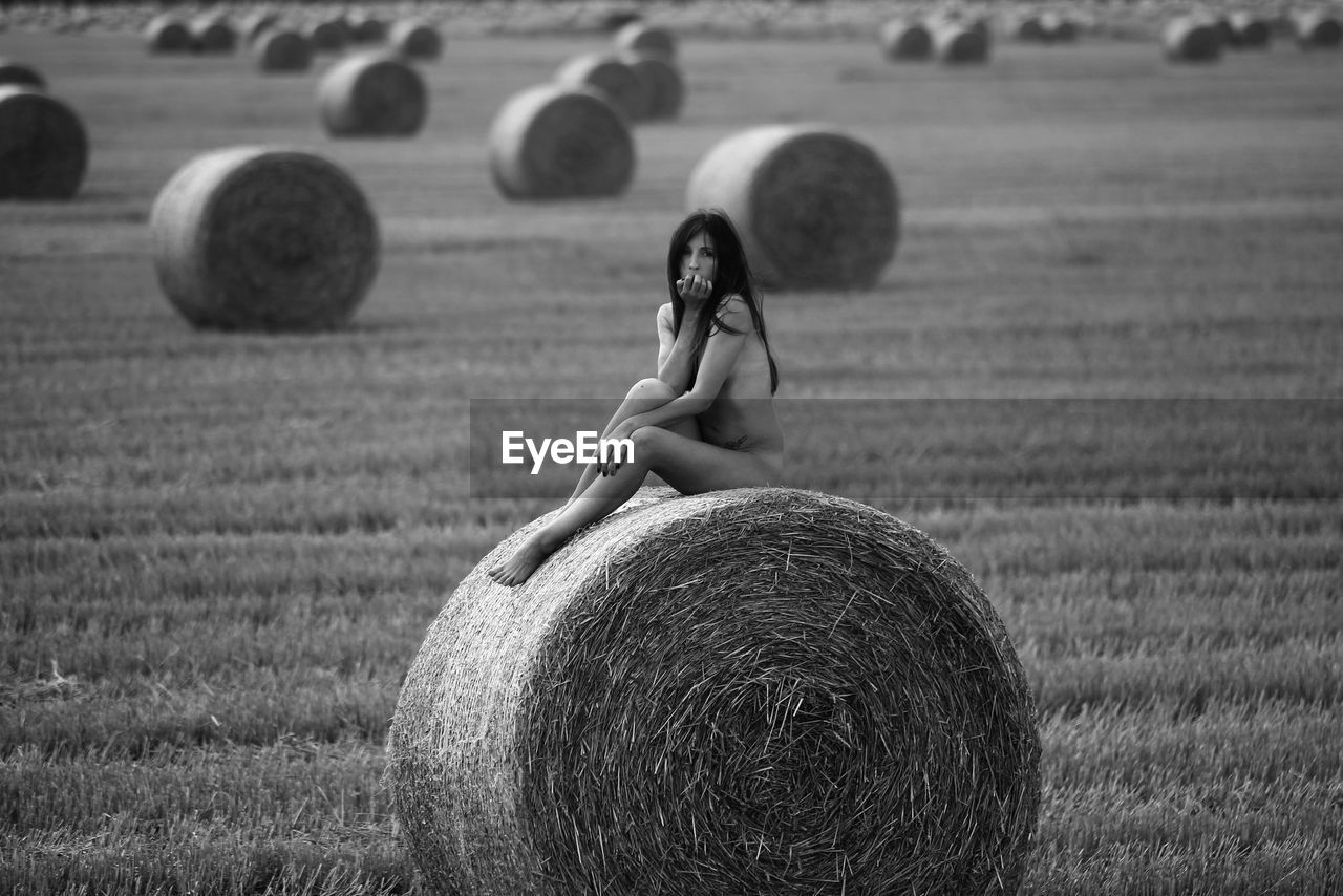 Sensuous naked woman sitting over hay bale on agricultural field
