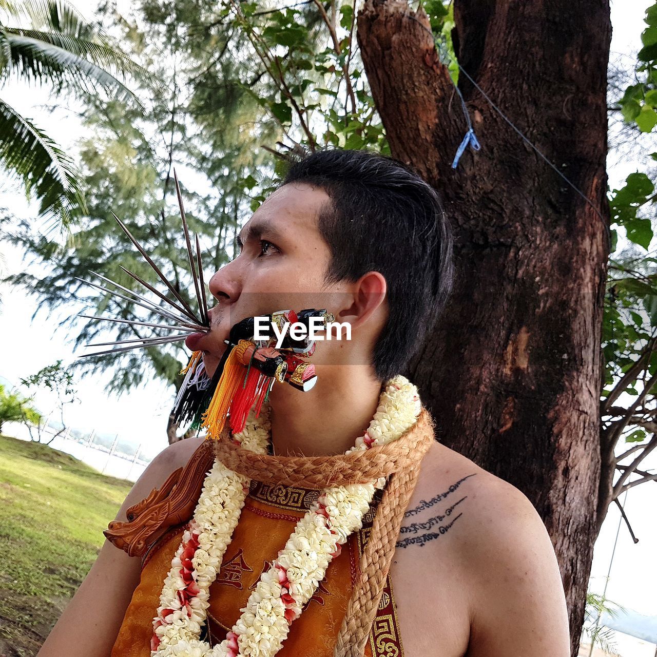 Close-up of young man with pierced mouth standing against tree trunk