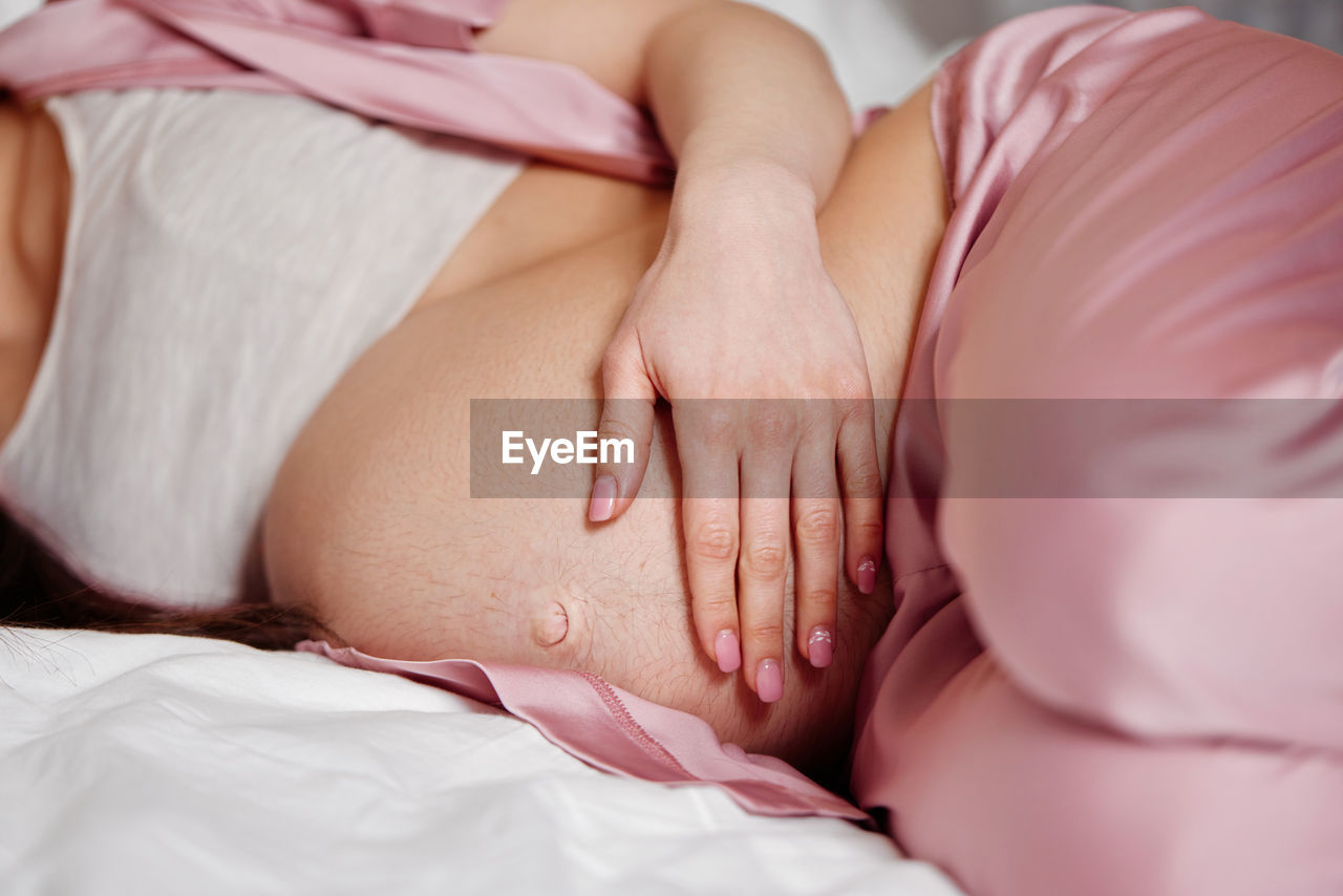 Midsection of pregnant woman sleeping on bed